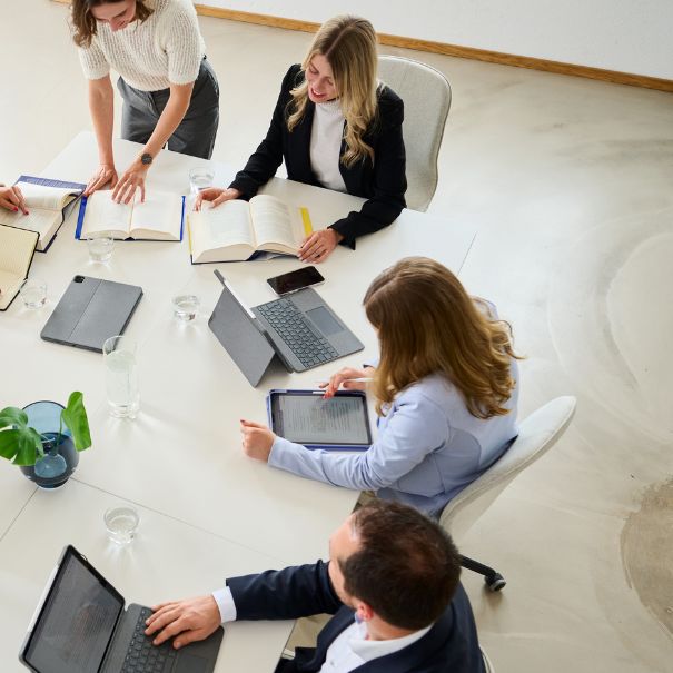 Vier Personen besprechen Dokumente an einem Konferenztisch mit digitalen Endger&auml;ten.